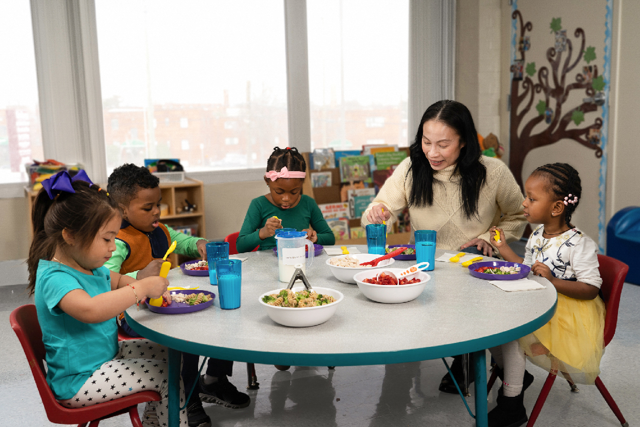 Children sharing a meal with support from a caregiver